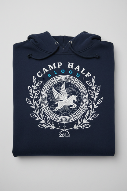 A navy blue folded hoodie with a white graphic print on the front. The graphic features a Pegasus emblem inside a circular frame with Greek key patterns, surrounded by a laurel wreath, with the text 'CAMP HALFT BLOOD' and '2013'.